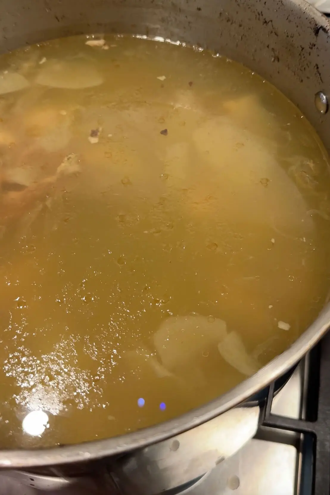 Rich and golden homemade chicken stock in a pot, made from scratch using chicken bones, garlic, and onions for a nutritious and flavorful broth.